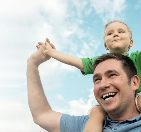A smiling father with his young child on his shoulders